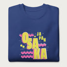 Folded royal blue sweatshirt with a vibrant graphic of the words "OSAKA JAPAN" in large yellow letters, surrounded by pink zigzag lines.