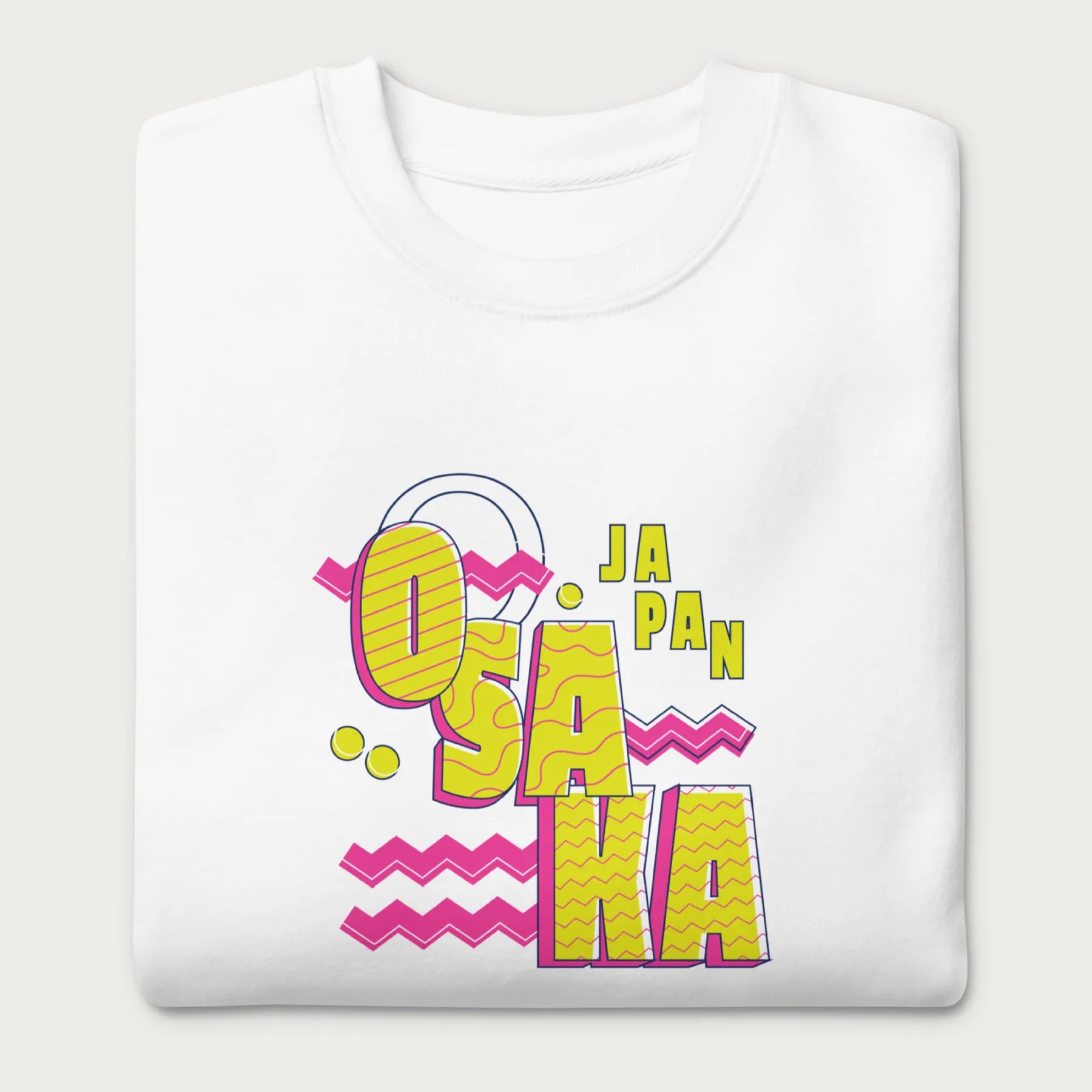 Folded white sweatshirt with a vibrant graphic of the words "OSAKA JAPAN" in large yellow letters, surrounded by pink zigzag lines.