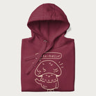 Folded maroon hoodie with graphic of a cute mushroom waving and the text "Porto-hello!"