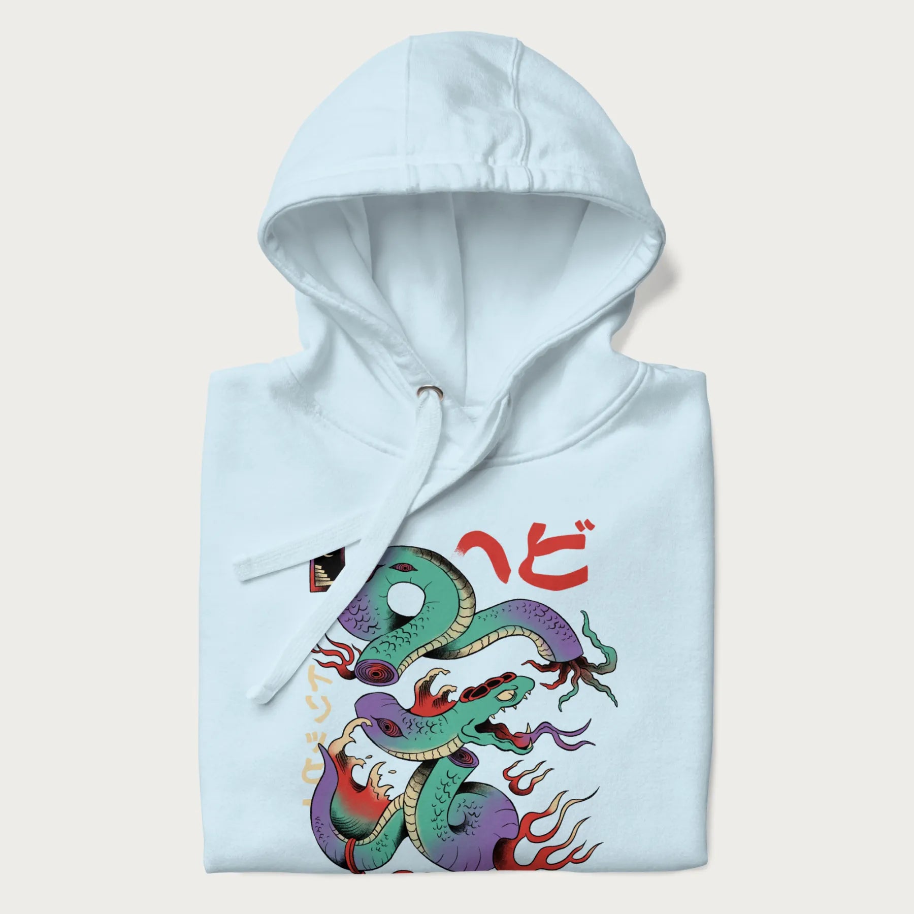 Folded light blue hoodie with Japanese psychedelic snake graphic, with Japanese text 'ヘビ' (Snake) and 'トリッピー' (Trippy) in vibrant colors.