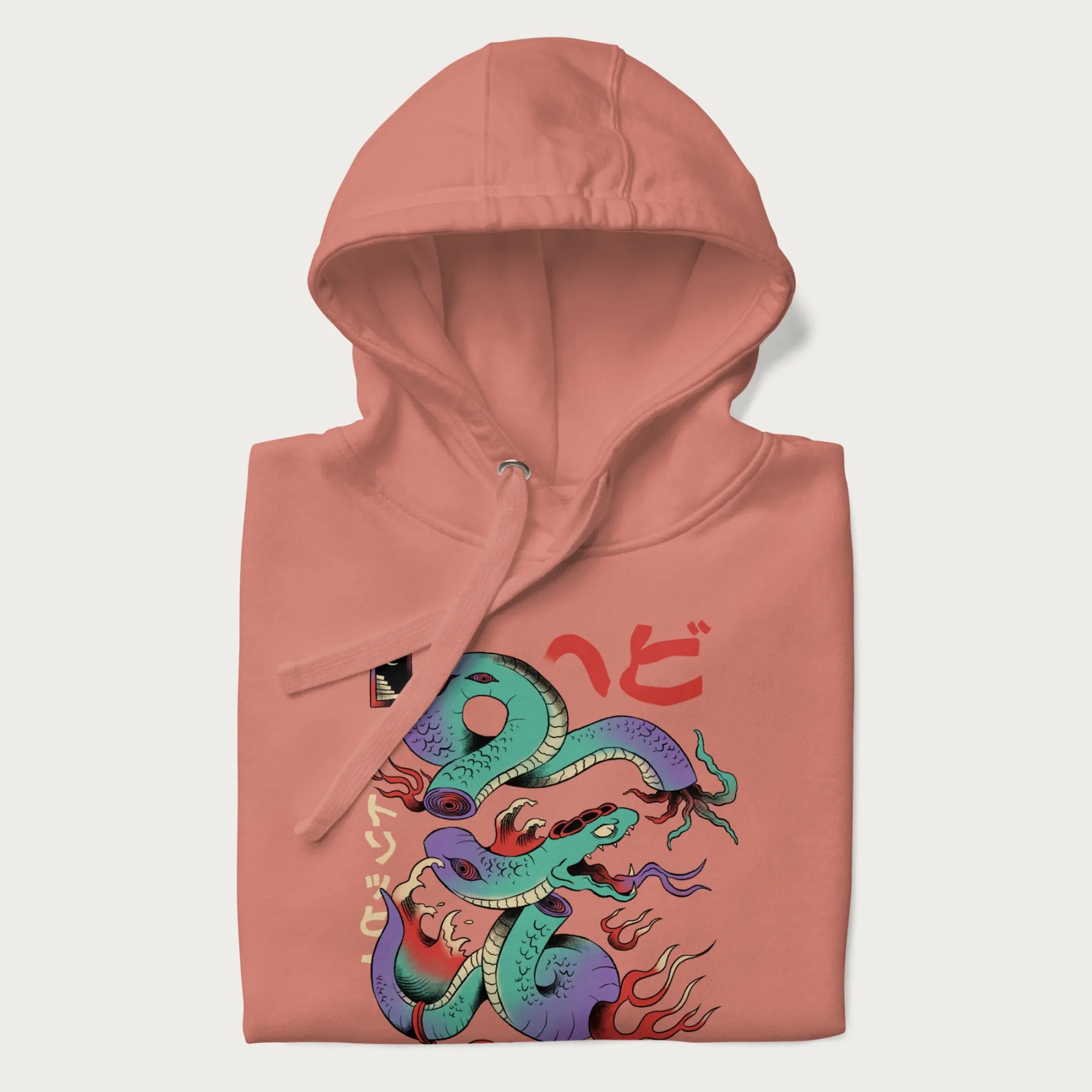 Folded light pink hoodie with Japanese psychedelic snake graphic, with Japanese text 'ヘビ' (Snake) and 'トリッピー' (Trippy) in vibrant colors.