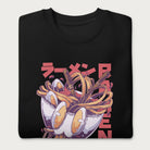 Folded black sweatshirt with a vibrant graphic of a bowl of ramen noodles, depicted in a dynamic, cartoonish style with bold Japanese text.