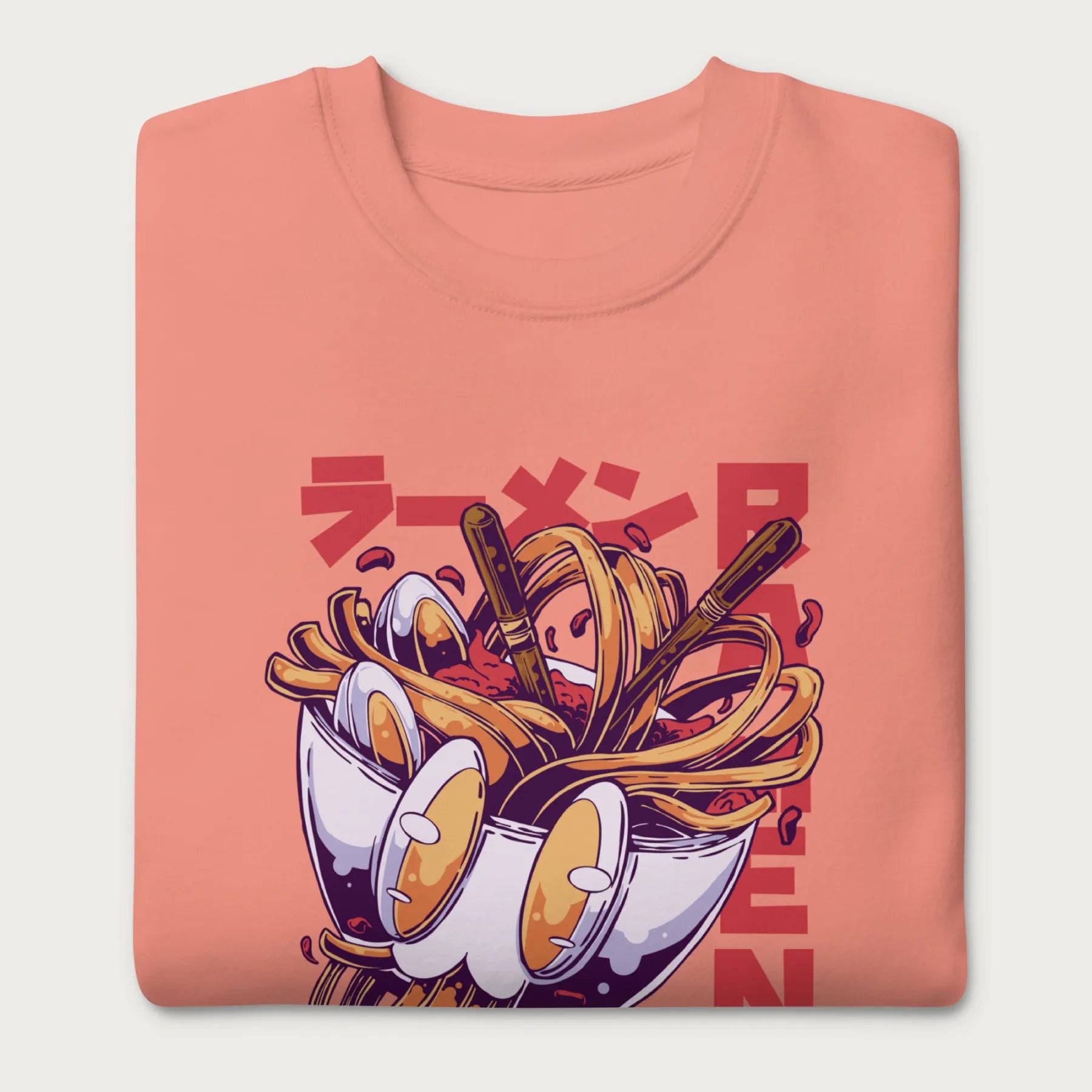 Folded light pink sweatshirt with a vibrant graphic of a bowl of ramen noodles, depicted in a dynamic, cartoonish style with bold Japanese text.