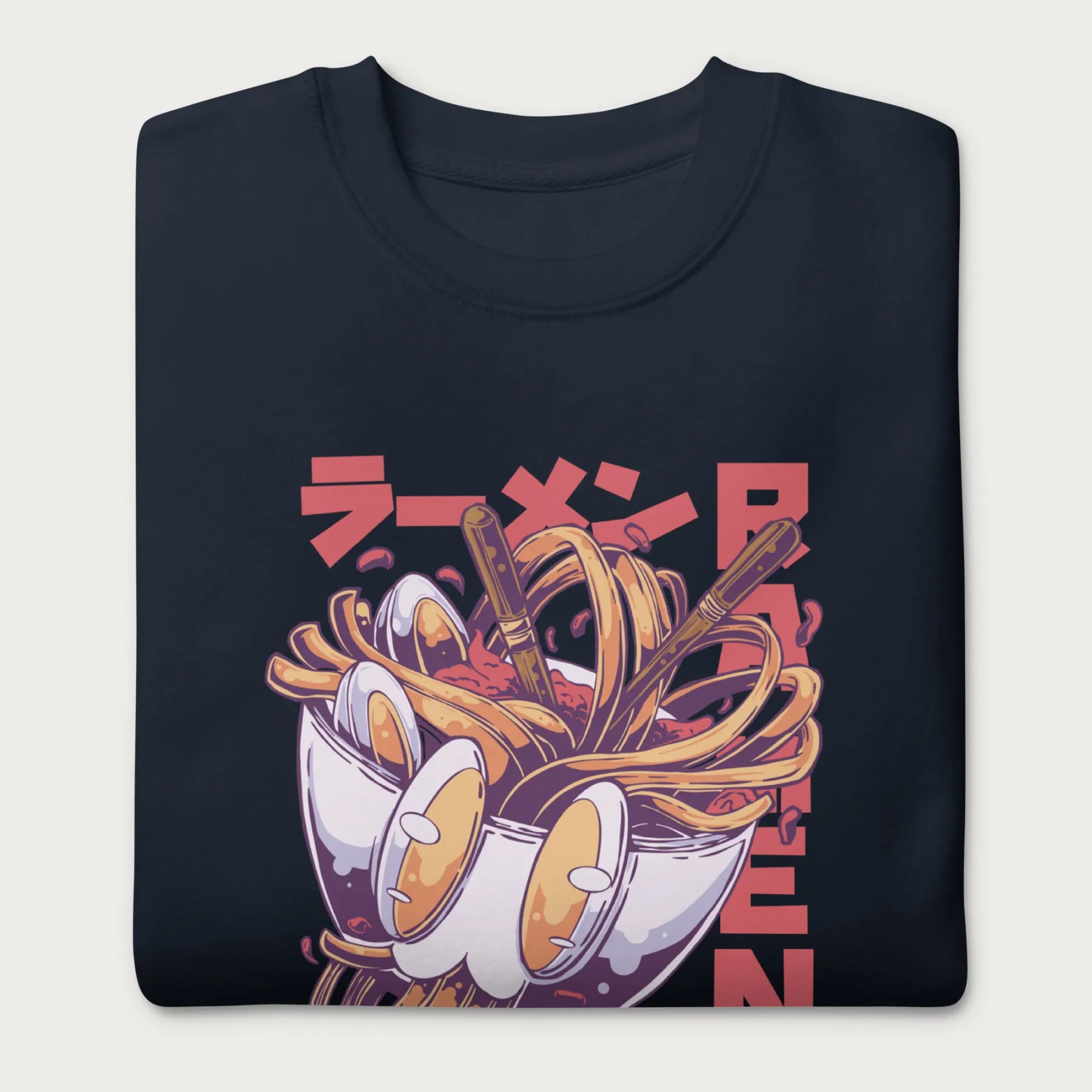 Folded navy blue sweatshirt with a vibrant graphic of a bowl of ramen noodles, depicted in a dynamic, cartoonish style with bold Japanese text.