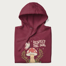 Folded maroon hoodie with mushroom and butterfly design, with the text 'Respect the Soil' above it. 