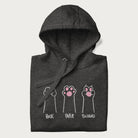 Folded dark grey hoodie with graphic of cat paws playing rock-paper-scissors.