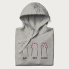 Folded light grey hoodie with graphic of cat paws playing rock-paper-scissors.