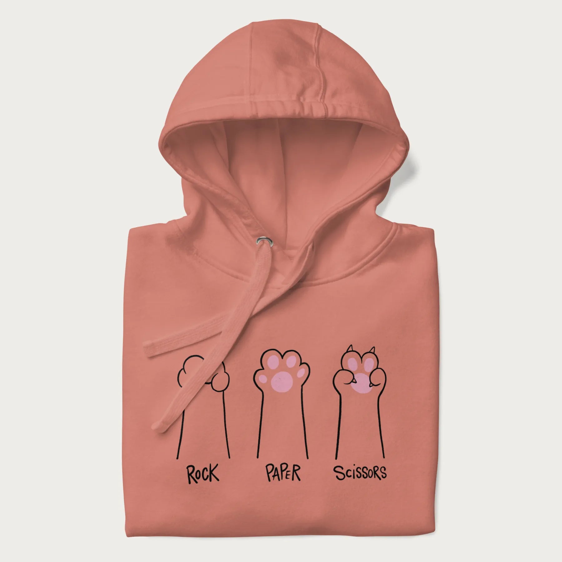 Folded light pink hoodie with graphic of cat paws playing rock-paper-scissors.