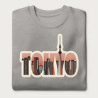 Folded light grey sweatshirt with a graphic of Tokyo's skyline integrated within the letters spelling "TOKYO."