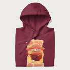 Folded maroon hoodie with a graphic of a character with a mushroom cap playing a guitar and the text 'Stay Trippy Little Hippie.'