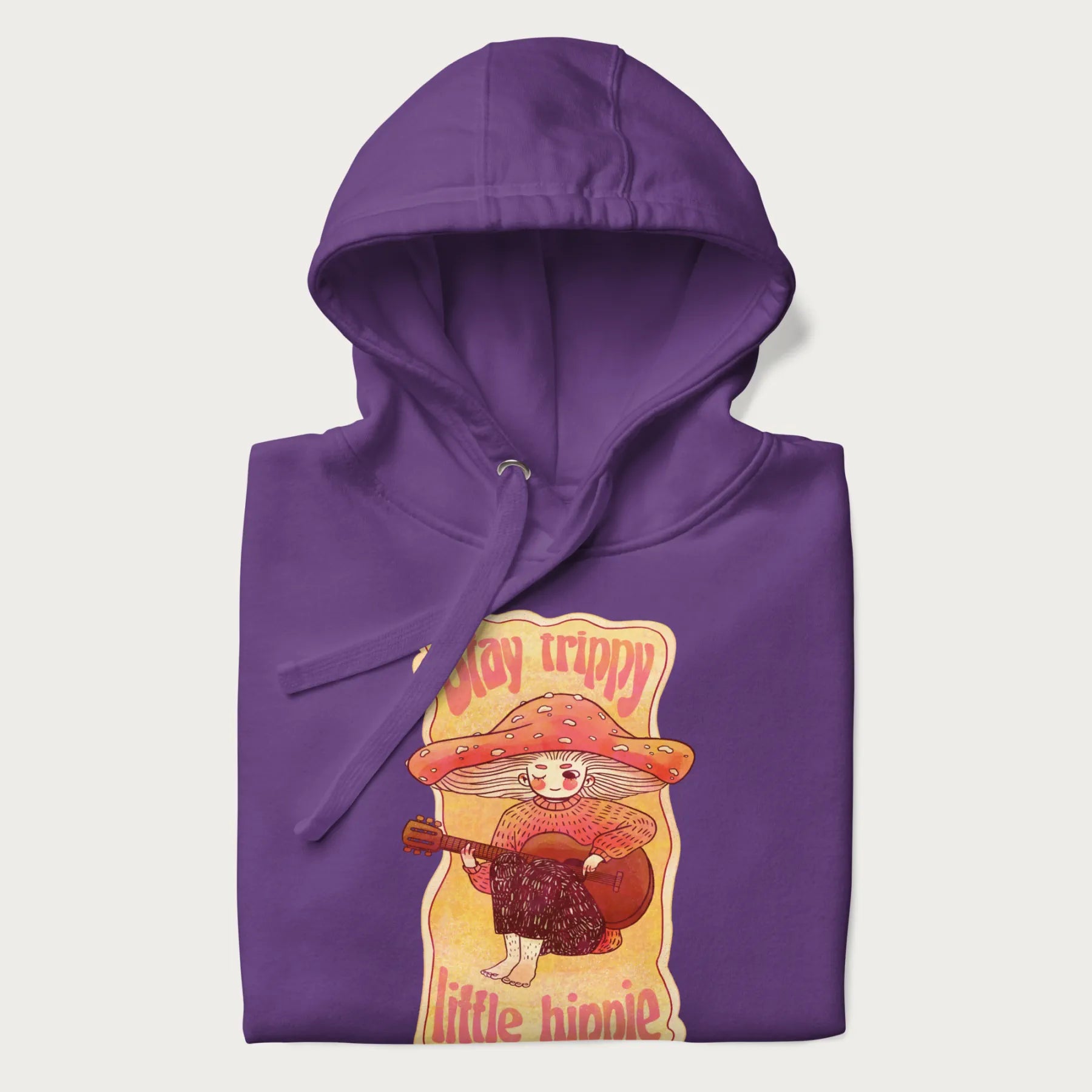 Folded purple hoodie with a graphic of a character with a mushroom cap playing a guitar and the text 'Stay Trippy Little Hippie.'