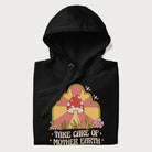 Folded black hoodie with a graphic of a happy red mushroom, sunburst background, and the text 'Take Care of Mother Earth'.