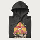 Folded dark grey hoodie with a graphic of a happy red mushroom, sunburst background, and the text 'Take Care of Mother Earth'.