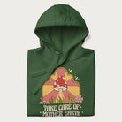 Folded forest green hoodie with a graphic of a happy red mushroom, sunburst background, and the text 'Take Care of Mother Earth'.