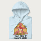 Folded light blue hoodie with a graphic of a happy red mushroom, sunburst background, and the text 'Take Care of Mother Earth'.