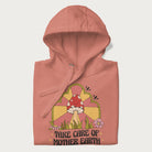 Folded light pink hoodie with a graphic of a happy red mushroom, sunburst background, and the text 'Take Care of Mother Earth'.