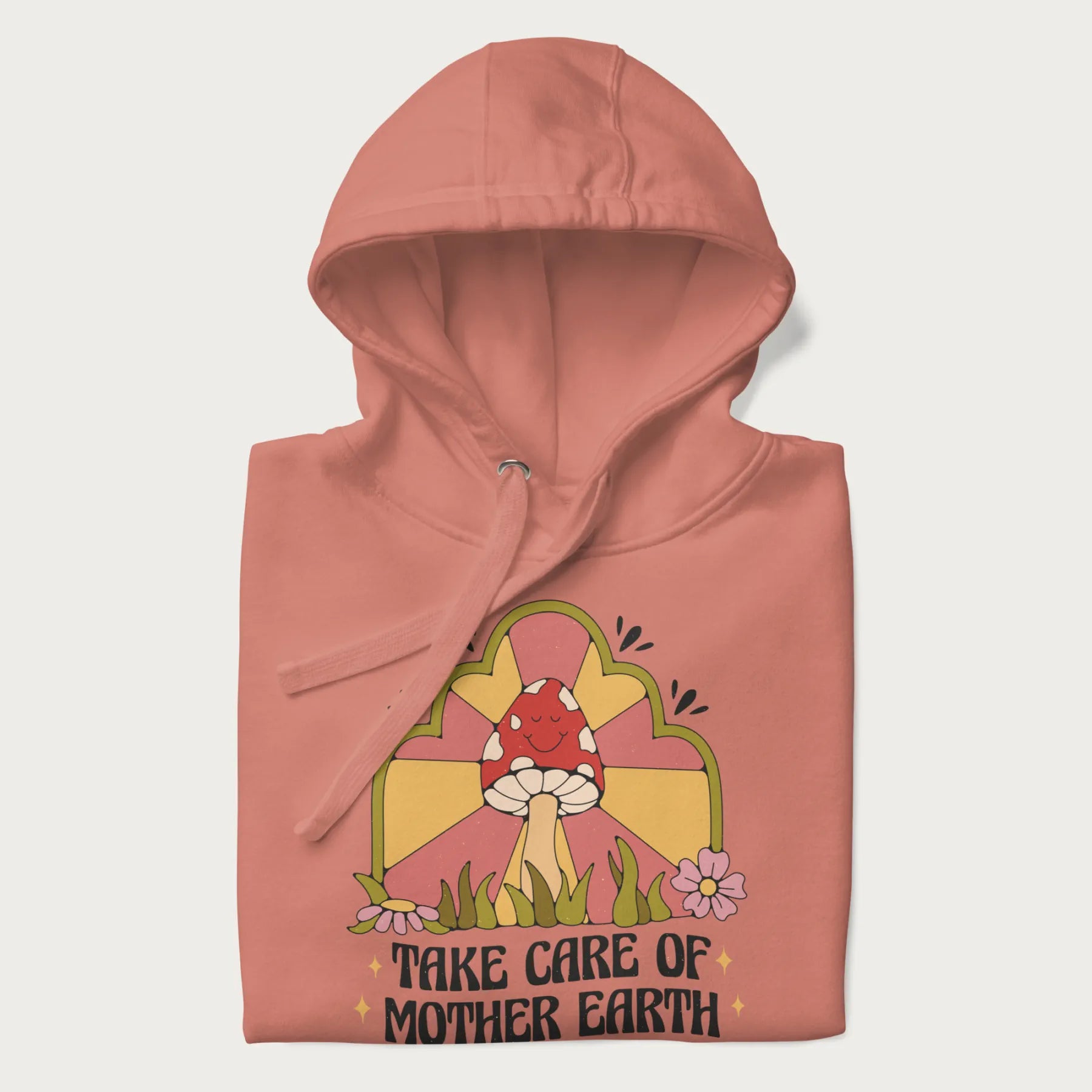 Folded light pink hoodie with a graphic of a happy red mushroom, sunburst background, and the text 'Take Care of Mother Earth'.