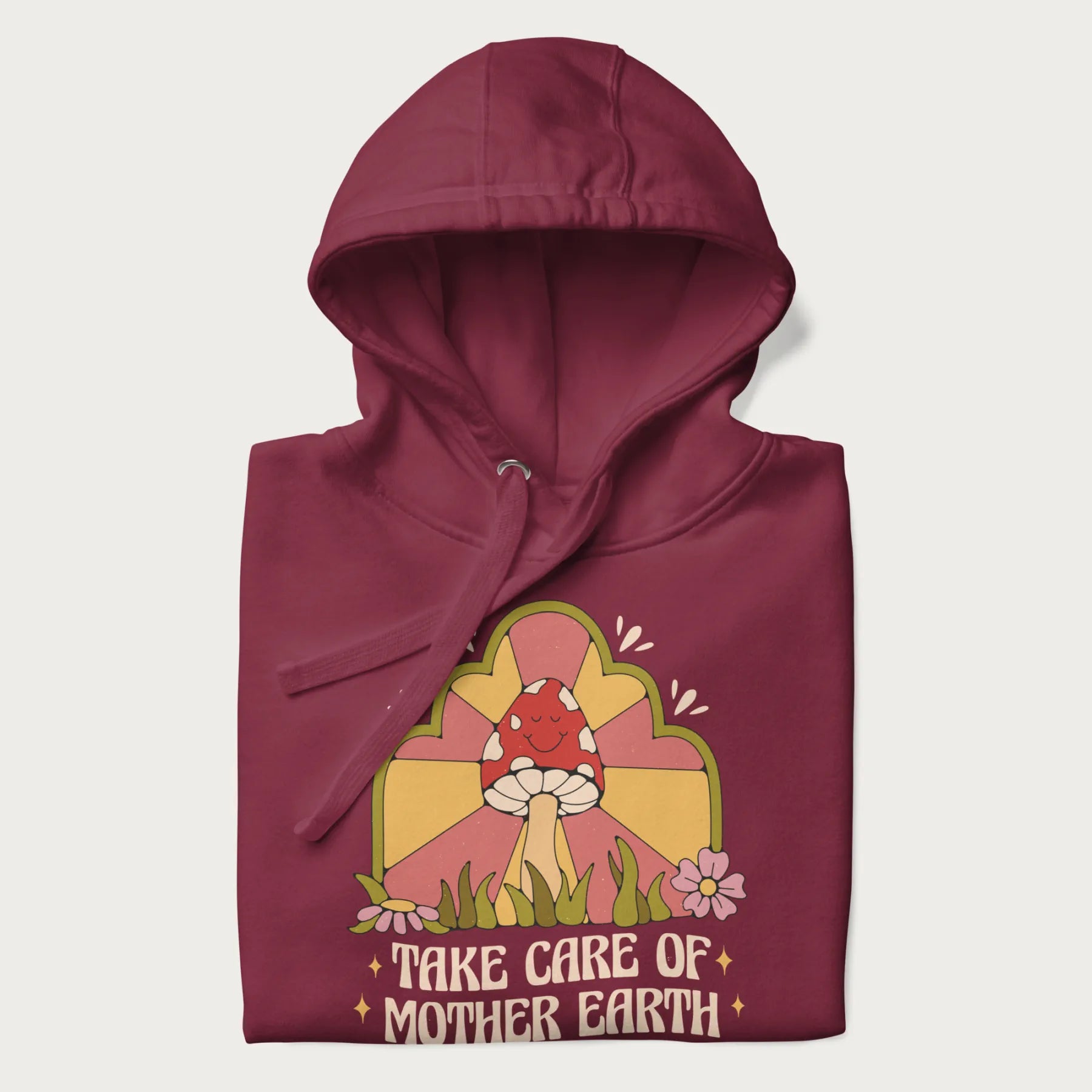 Folded maroon hoodie with a graphic of a happy red mushroom, sunburst background, and the text 'Take Care of Mother Earth'.