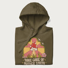 Folded military green hoodie with a graphic of a happy red mushroom, sunburst background, and the text 'Take Care of Mother Earth'.