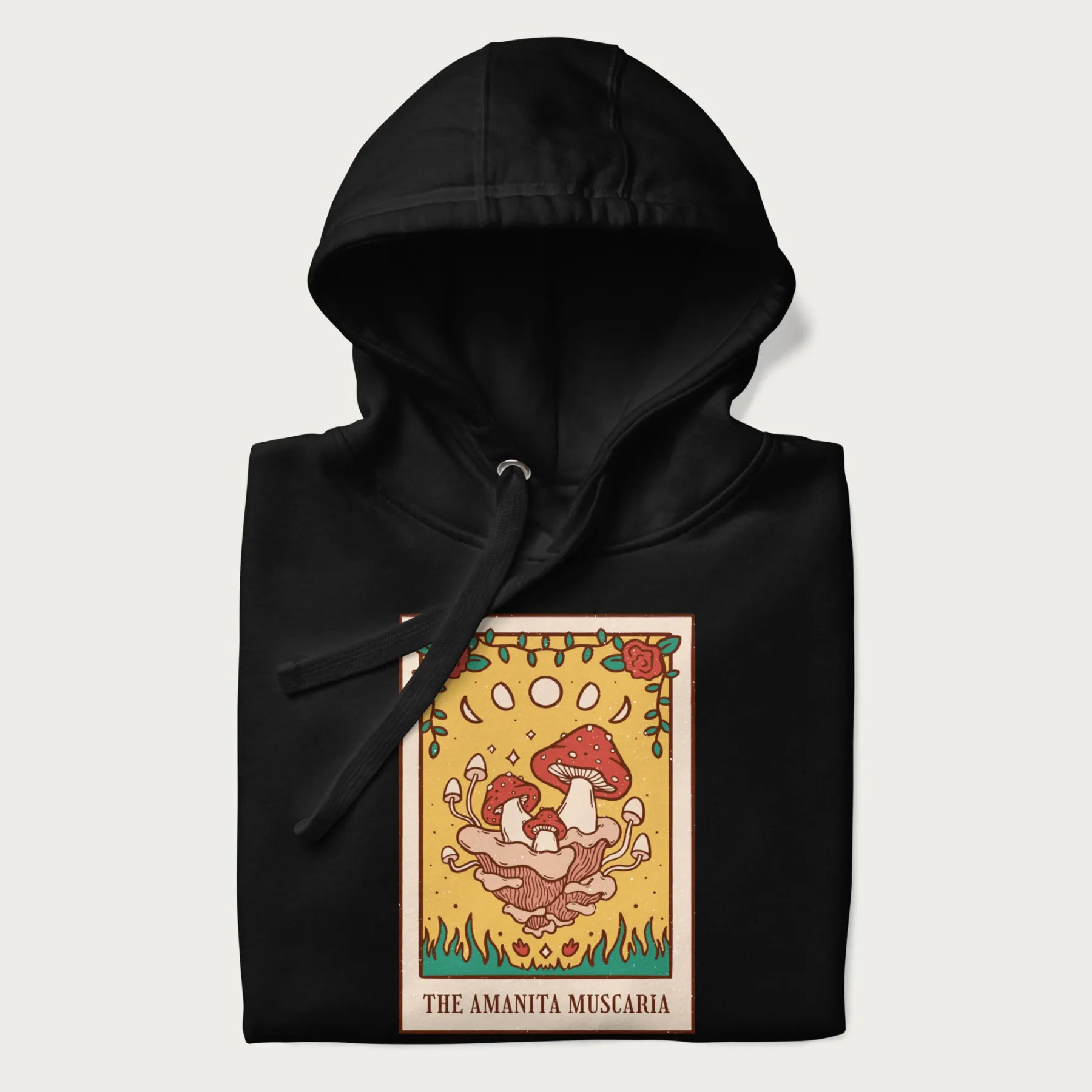 Folded black hoodie featuring a graphic of Amanita Muscaria mushrooms with floral accents and moon phases, resembling a tarot card.