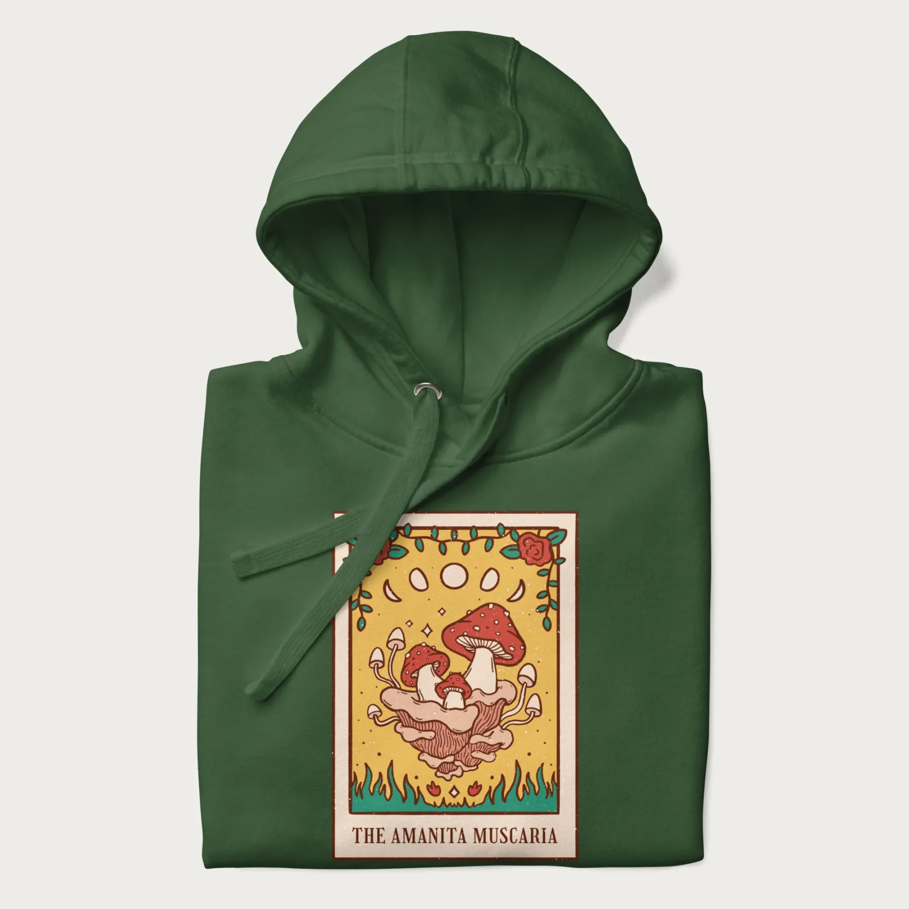 Folded forest green hoodie featuring a graphic of Amanita Muscaria mushrooms with floral accents and moon phases, resembling a tarot card.