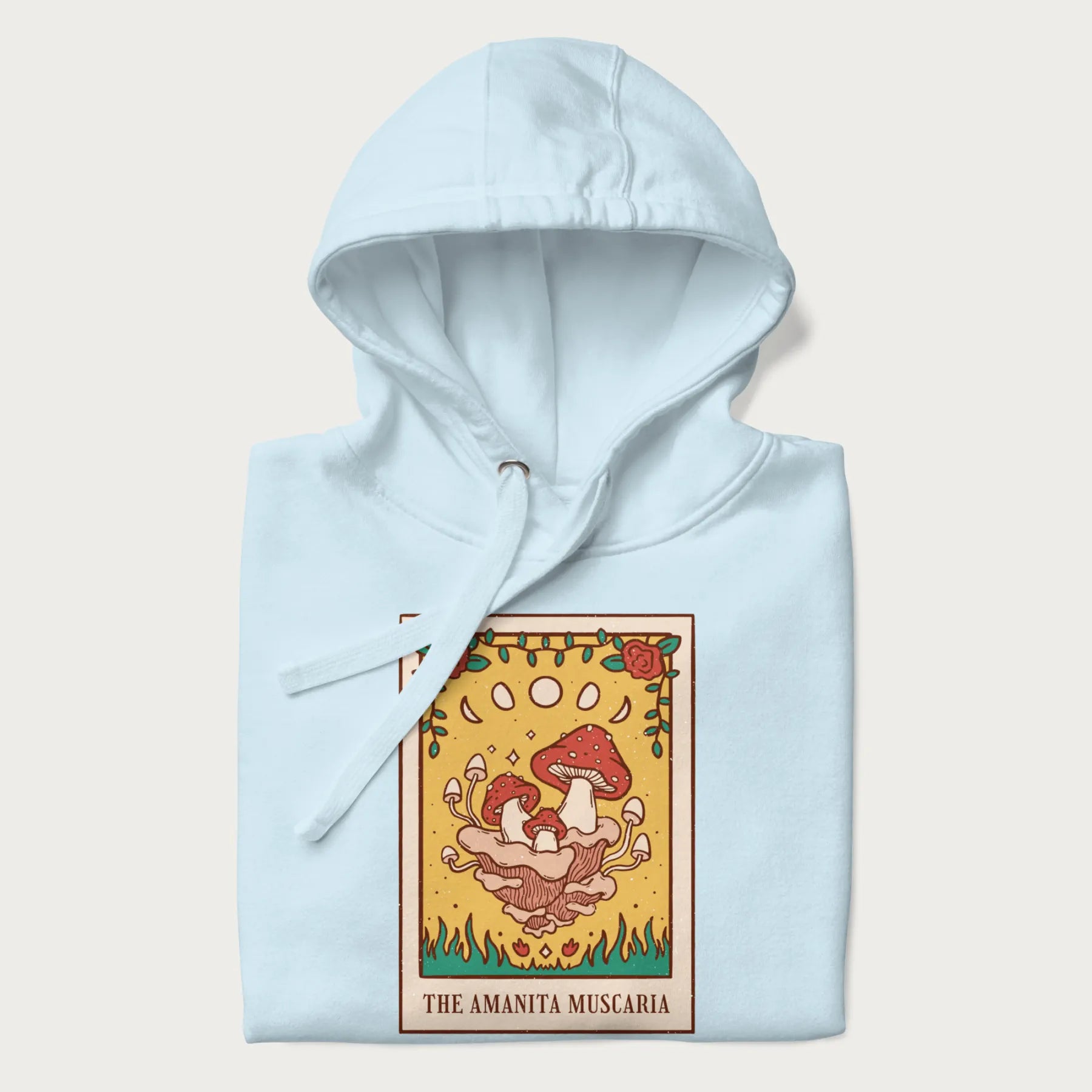 Folded light blue hoodie featuring a graphic of Amanita Muscaria mushrooms with floral accents and moon phases, resembling a tarot card.