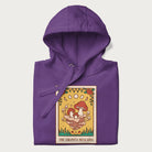 Folded purple hoodie featuring a graphic of Amanita Muscaria mushrooms with floral accents and moon phases, resembling a tarot card.