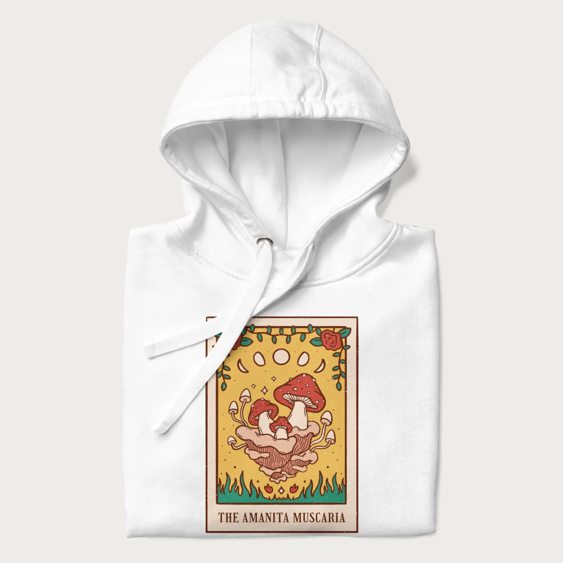 Folded white hoodie featuring a graphic of Amanita Muscaria mushrooms with floral accents and moon phases, resembling a tarot card.