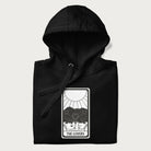 Folded black hoodie with a 'The Lovers' tarot card graphic of two cats with intertwined tails forming a heart, wine, and roses.