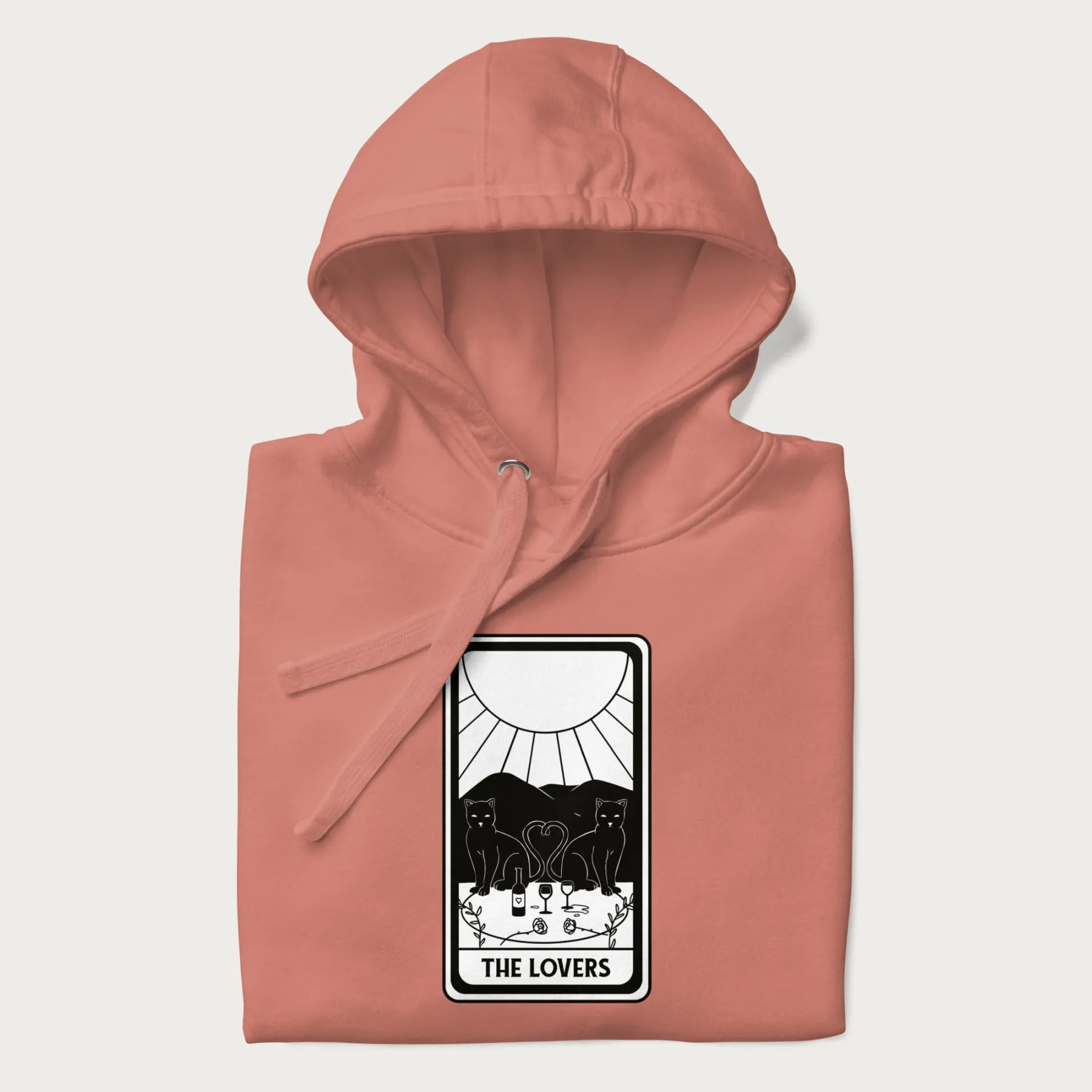 Folded light pink hoodie with a 'The Lovers' tarot card graphic of two cats with intertwined tails forming a heart, wine, and roses.
