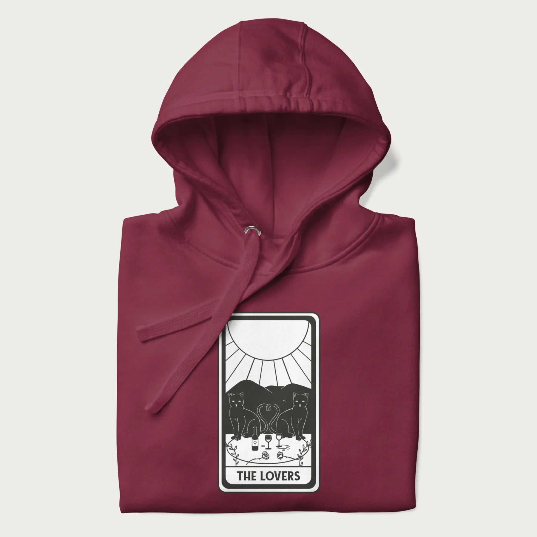 Folded maroon hoodie with a 'The Lovers' tarot card graphic of two cats with intertwined tails forming a heart, wine, and roses.