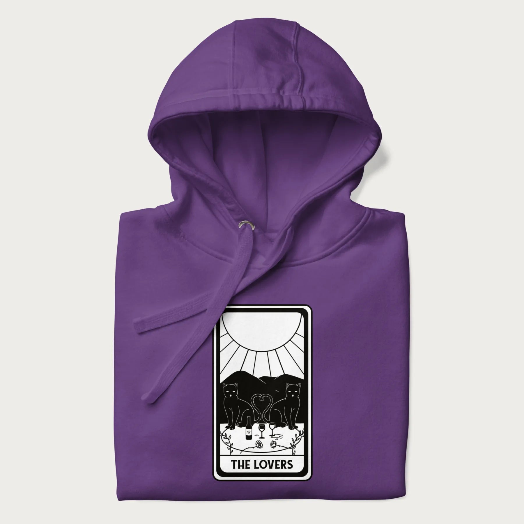 Folded purple hoodie with a 'The Lovers' tarot card graphic of two cats with intertwined tails forming a heart, wine, and roses.