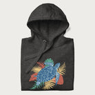 Folded dark grey hoodie with a vibrant graphic of a blue sea turtle and colorful tropical leaves.