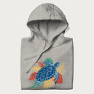 Folded light grey hoodie with a vibrant graphic of a blue sea turtle and colorful tropical leaves.