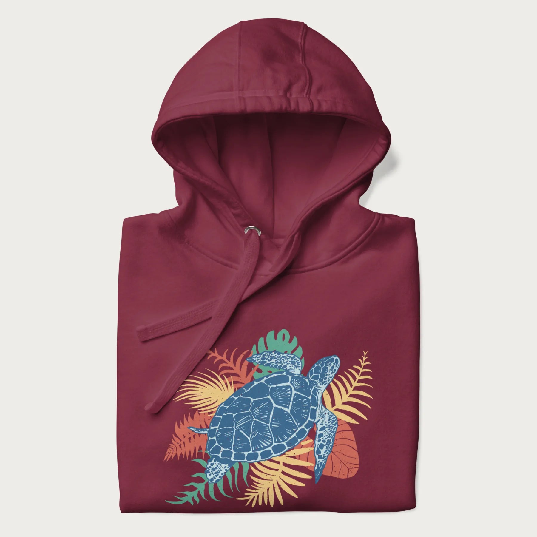 Folded maroon hoodie with a vibrant graphic of a blue sea turtle and colorful tropical leaves.