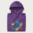 Folded purple hoodie with a vibrant graphic of a blue sea turtle and colorful tropical leaves.