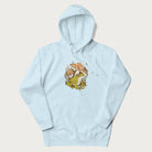 Light blue hoodie with cottagecore graphic of a frog under mushrooms with foliage in the background.