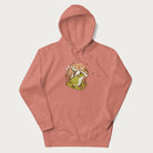 Light pink hoodie with cottagecore graphic of a frog under mushrooms with foliage in the background.