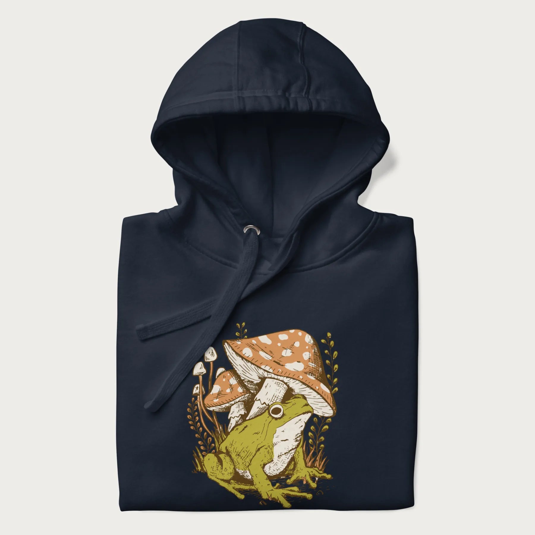 Folded navy blue hoodie with cottagecore graphic of a frog under mushrooms with foliage in the background.