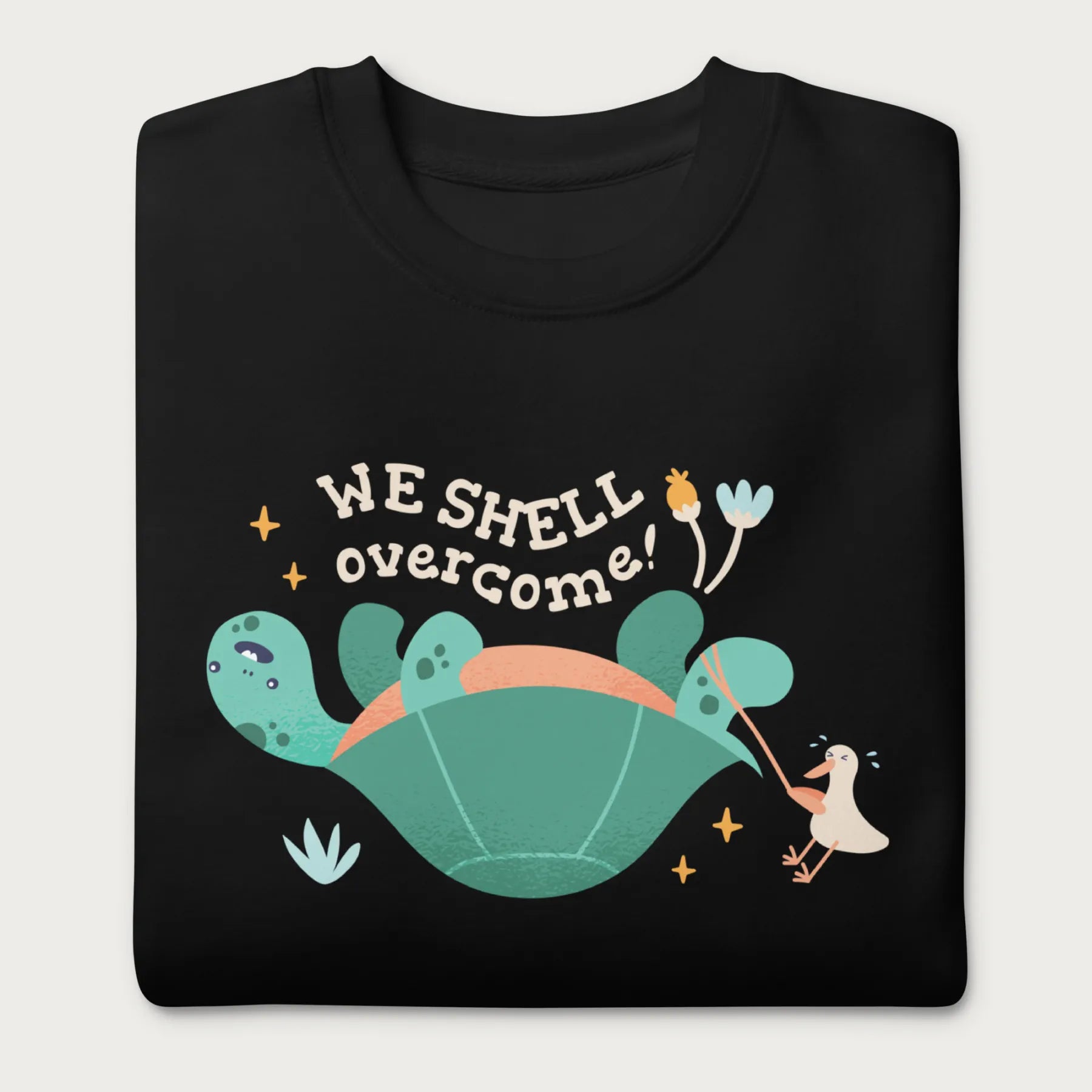 Folded black sweatshirt with a graphic of a turtle flipped on it's shell with the phrase 'We Shell Overcome.'