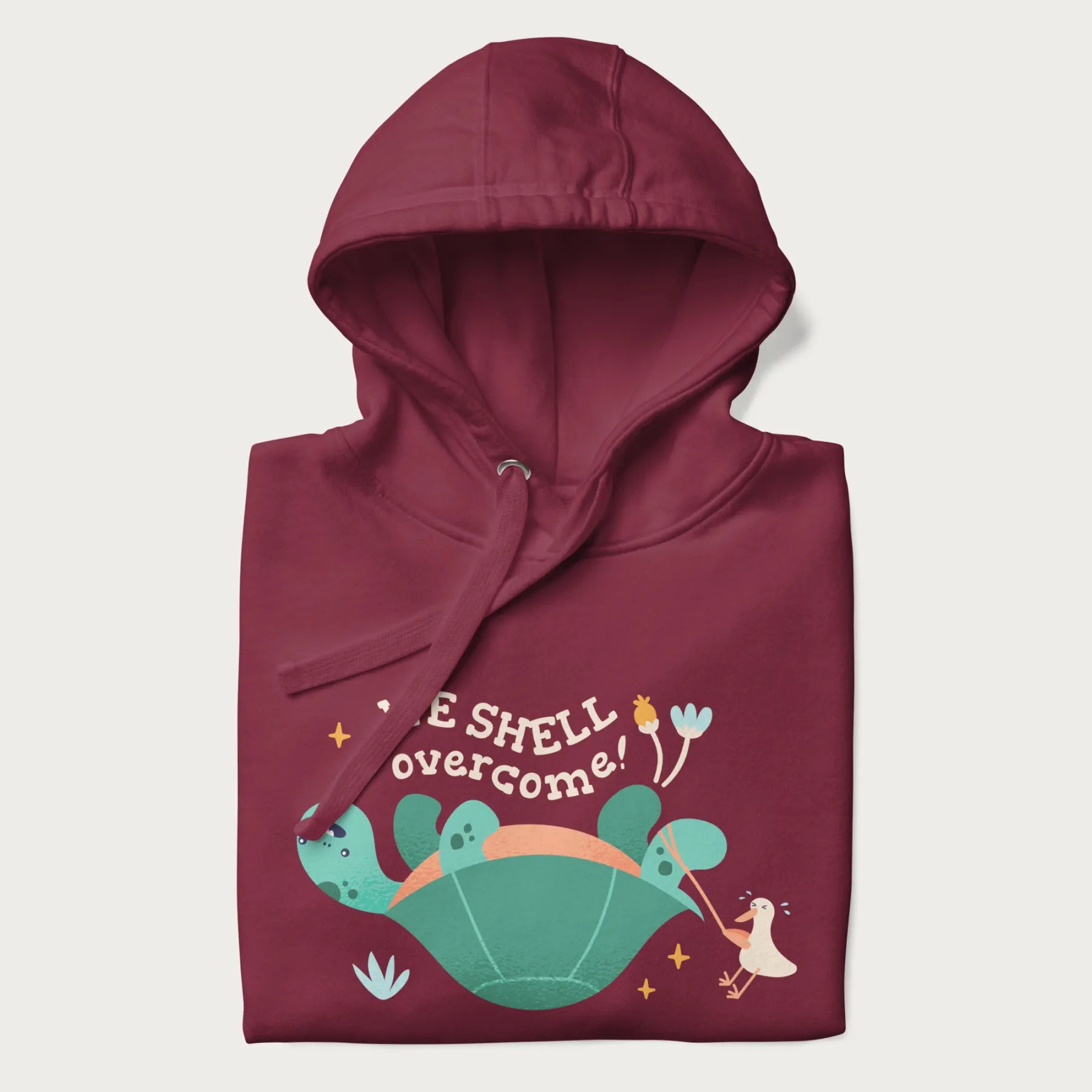 Folded maroon hoodie with graphic of a turtle and a duck with the text 'We Shell Overcome'.