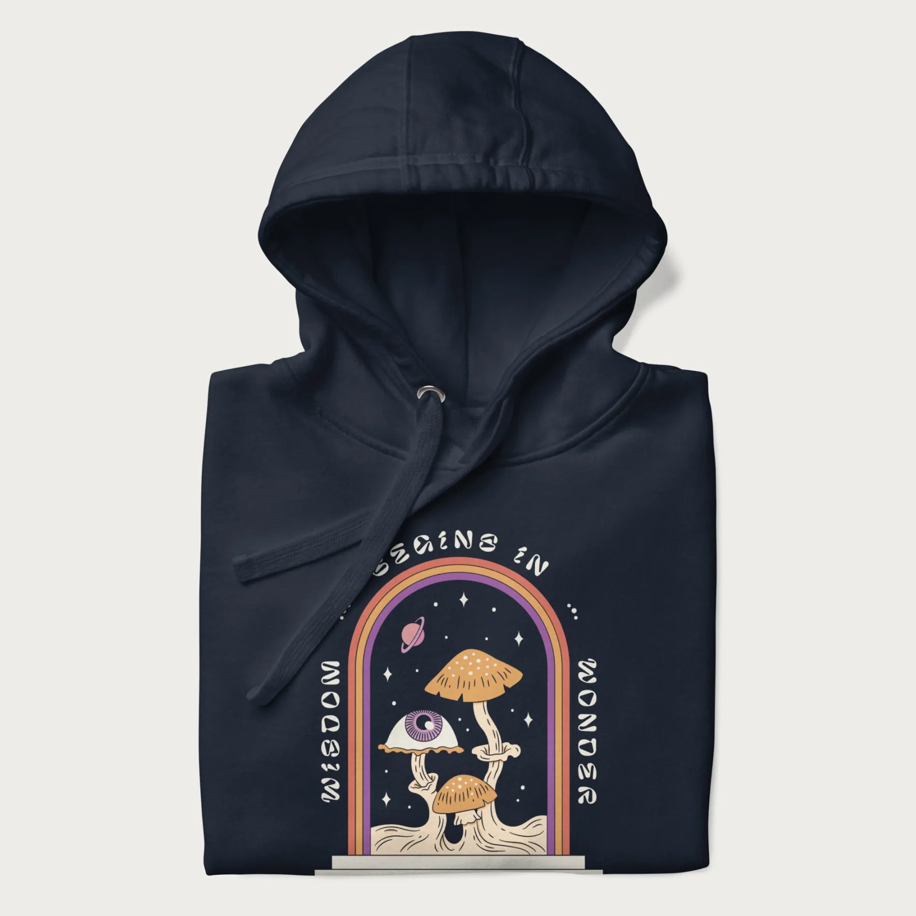 Folded navy blue hoodie with graphic of mystical mushrooms with an all-seeing eye and the text 'Wisdom Begins in Wonder' framed by a rainbow arch.