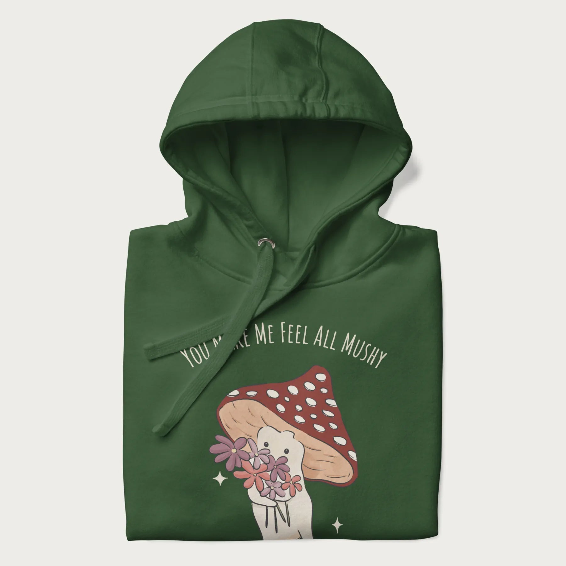 Folded forest green hoodie with graphic of a cute mushroom character holding a bouquet of flowers with the text 'You Make Me Feel All Mushy' above.