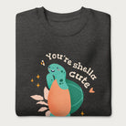 Folded dark grey sweatshirt with a cute graphic of a smiling turtle and bee with the phrase 'You're Shella Cute.'