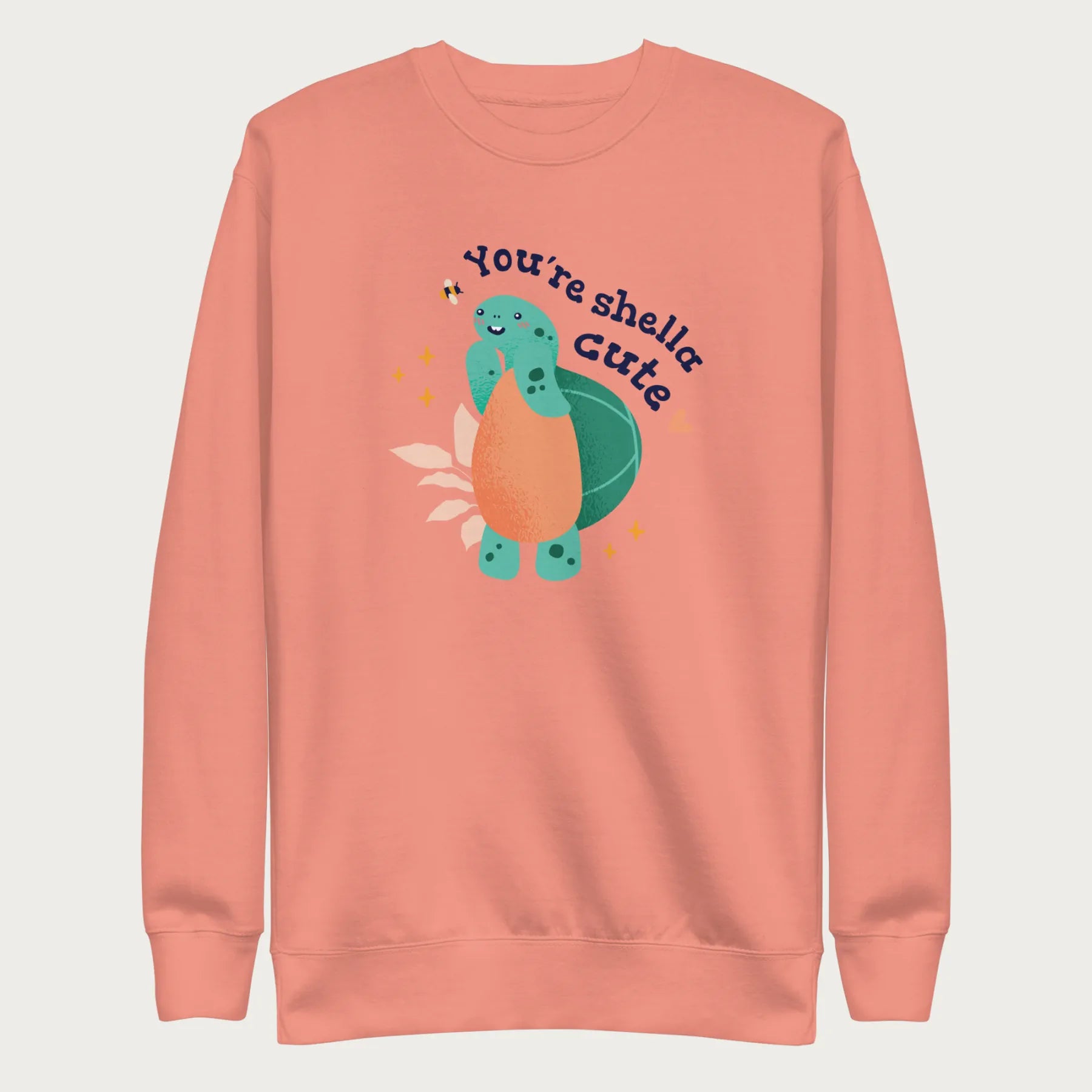 Light pink sweatshirt with a cute graphic of a smiling turtle and bee with the phrase 'You're Shella Cute.'