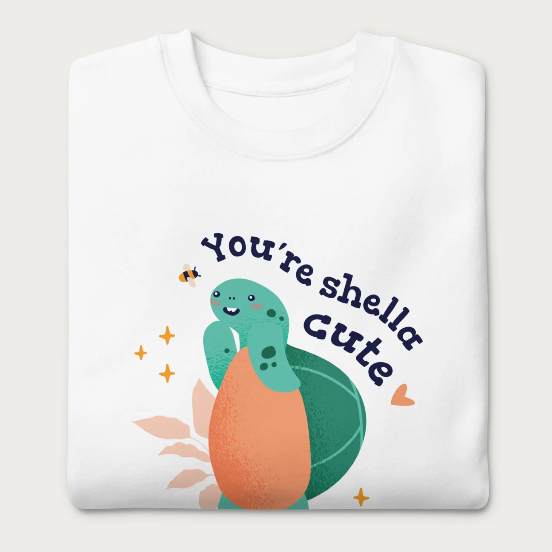 Folded white sweatshirt with a cute graphic of a smiling turtle and bee with the phrase 'You're Shella Cute.'